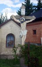 Uprosted obrzku stoj vklenkov kaplika ve patnm technickm stavu, ped n se ty krucifix s Jeem Kristem a npisem INRI. Ped kaplikou se nachz drtn plot. Vzadu je vidt zahrada se zelenm trvnkem a st rozestavnho domu.