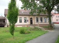 stedn motiv tvo jednopatrov budova bval koly, kter slo jako obecn ad. Na budov u dve jsou dva npisy obecn ad a mstn veejn knihovna. Nalevo se nachz devn zahrdka mstnho hostince. Napravo vzadu je vidt st budovy bvalho obchodu. Na trvnku ped budovou obecnho adu rostu kee a jeden vzrostl strom. Pravm spodnm okrajem vede mstn komunikace a od n se oddluje schodit smujc do budovy adu.