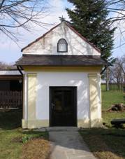 Kaplika Panny Marie Bolestn (pohled z ulice U Kaple) obklopen vzrostlmi listnatmi stromy. Za kapl roste jeden jehlinat strom. Vpravo ped kaplikou jsou dv devn laviky. Ke kapli vede betonov pstupov cesta, v jejm okol se nachz trvnk. Vlevo od kapliky a zleva za n je plot zahrady, v n je za kapl umstna jednopodlan gar s otevenmi vraty.